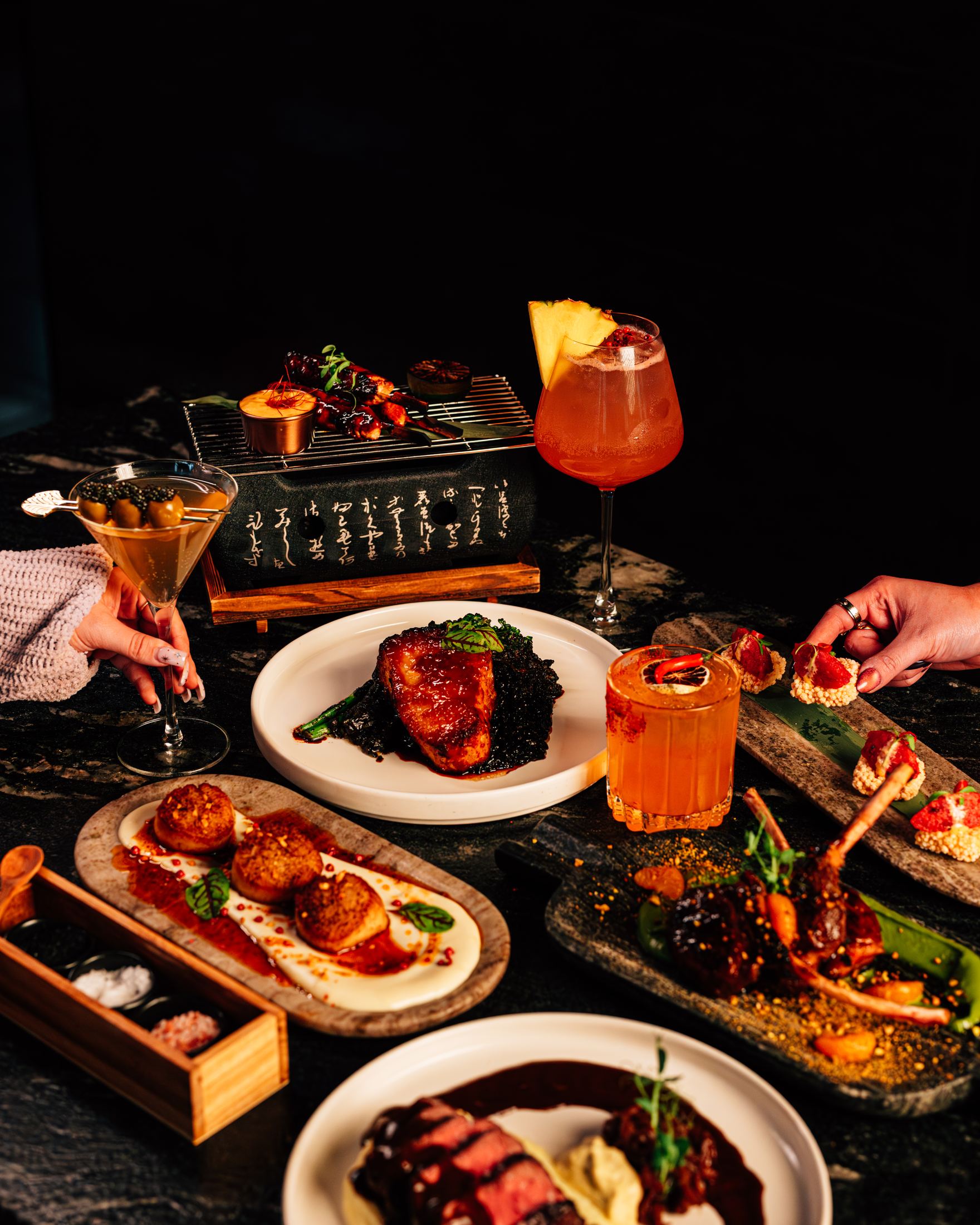 The table laid with dishes and cocktails, hands reaching in
