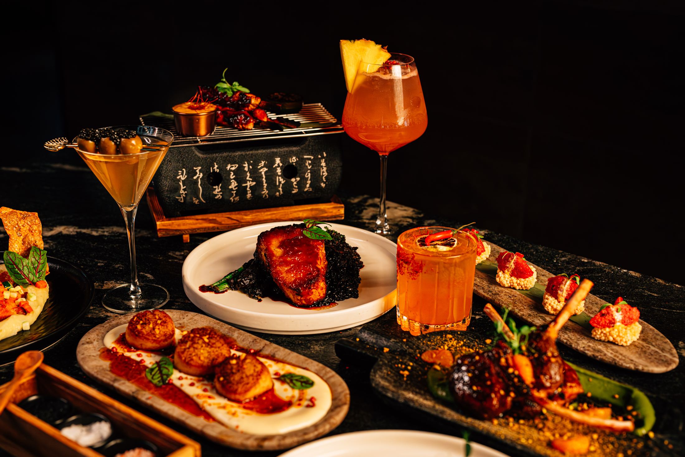 The table laid with dishes and cocktails across dark stone